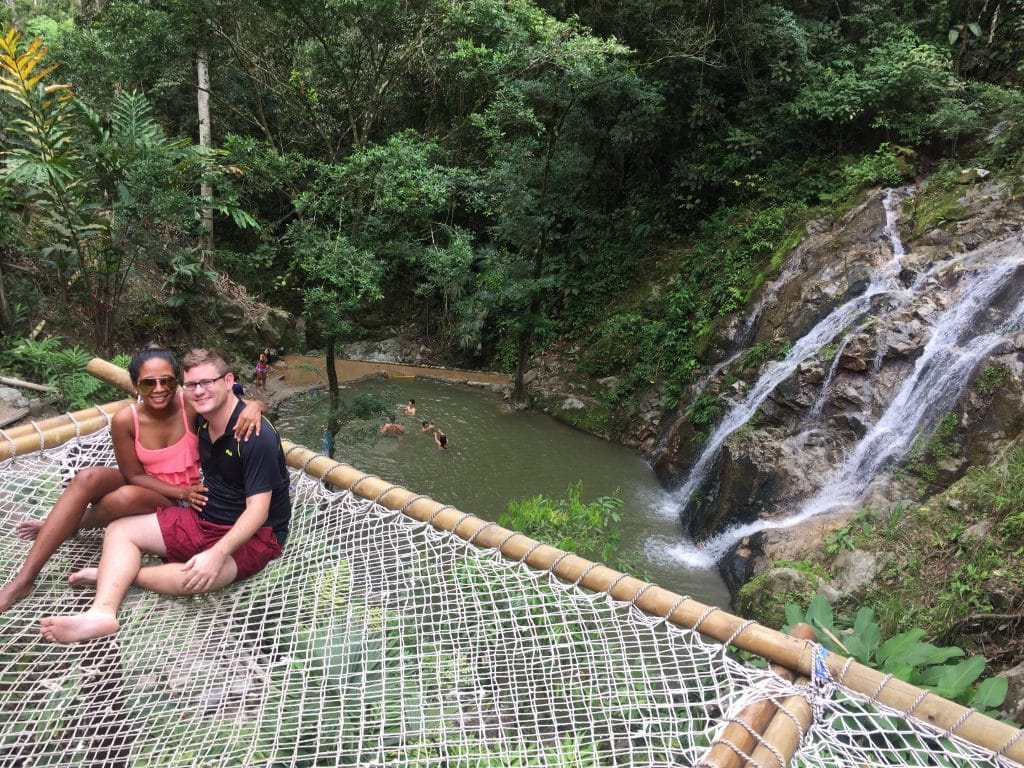 Adam and Susana sitting on a giant hammock overlooking the Marinka Waterfall, one of the best things to do in Minca, Colombia.