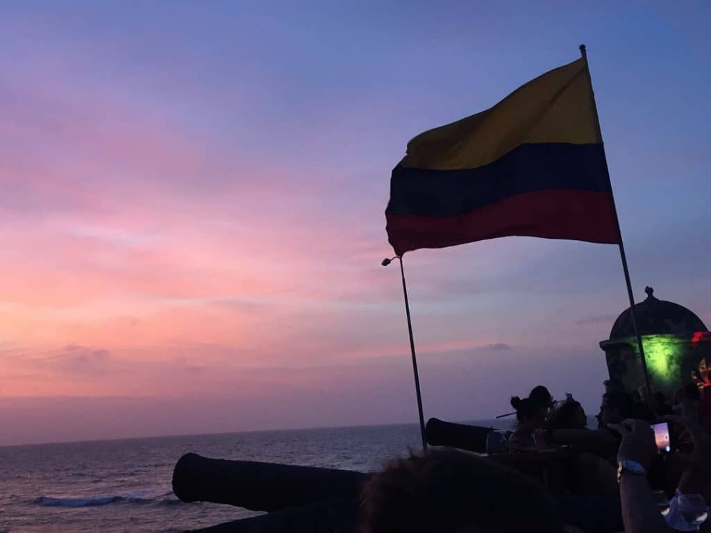 Photo of sunset from Café del Mar with a Colombian flag and sunset over the sea, another one of the must things to do in Colombia Cartagena