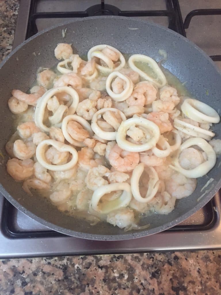 Foto de la preparción de los calamares y camarones al ajillo caseros en un sarten.