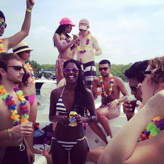 Photo of people sitting and standing on a boat, some with party necklaces and drinking beers.