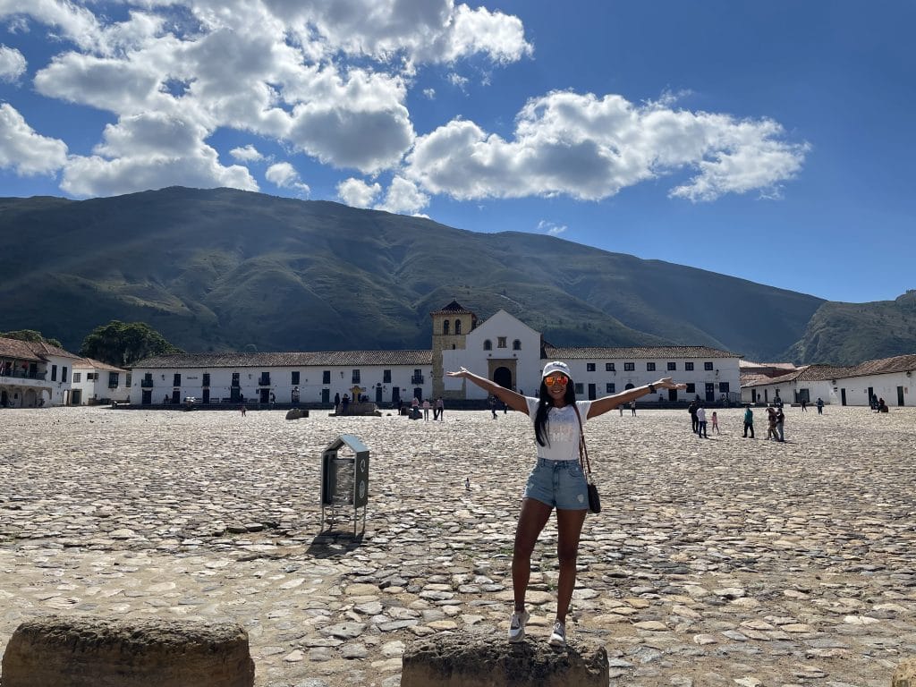 A girl standing with her arms raised with the plaza and church in Villa de Leyva, Colombia in the background.