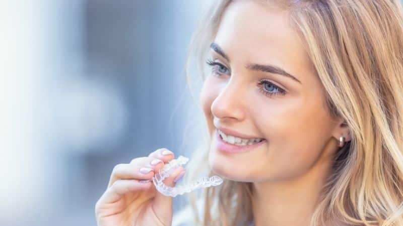 Photo of a girl smiling and holding her invisible aligner, something she could have gotten done while doing dental tourism in Colombia.