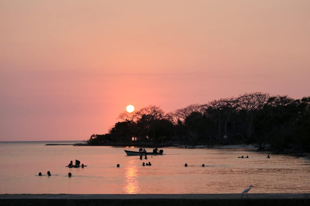 Photo of the sunset over the water and trees with people in the water at one of the Rosario Islands hotels.
