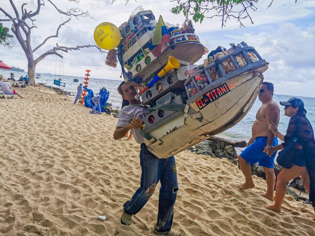 Foto de un vendedor con un barco grande con sus productos en una playa en Cartagena.