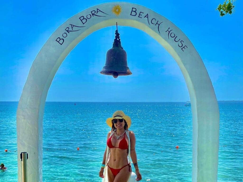 Photo of a girl under an archway with a bell in front of the water at beach club Bora Bora Beach Cartagena.