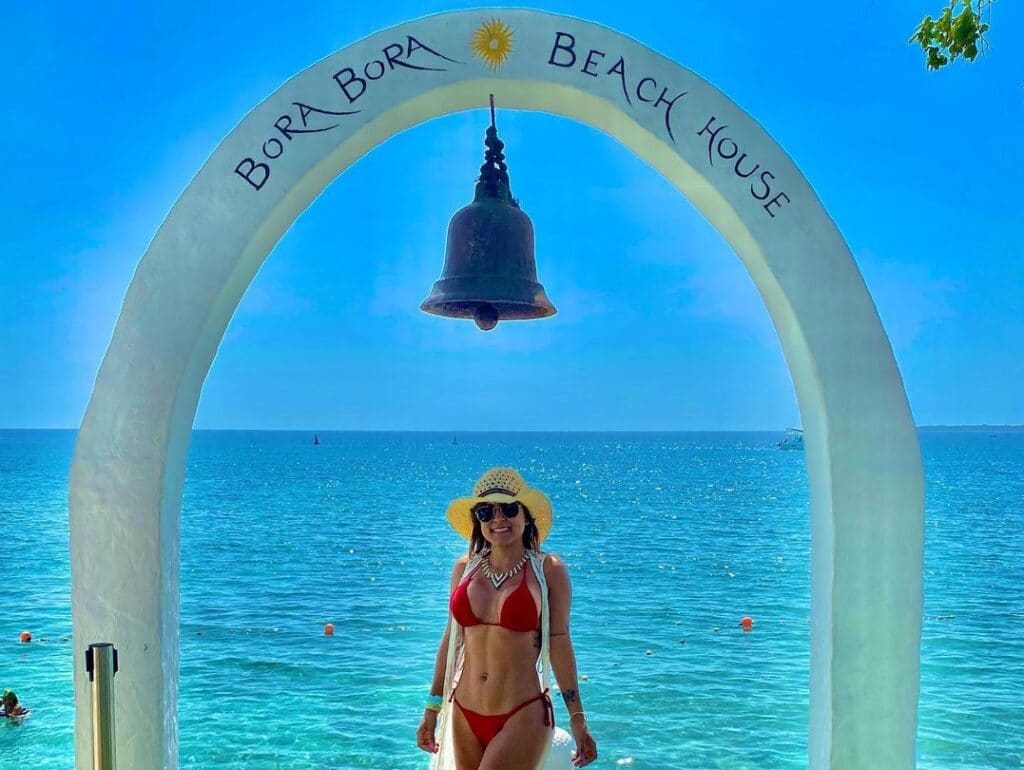Foto de una mujer debajo un arco con el mar atras.