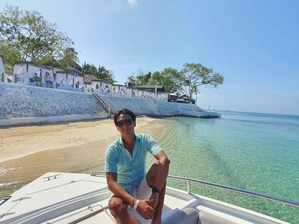 Foto de un hombre en el frente de un bote con una playa en el fondo.