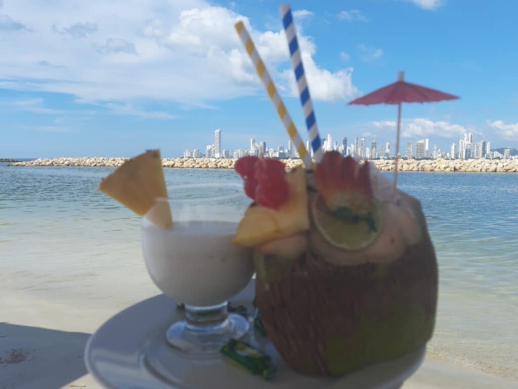 Foto de una bebida en copa y una en un coco enfrente de la playa de Cartagena.
