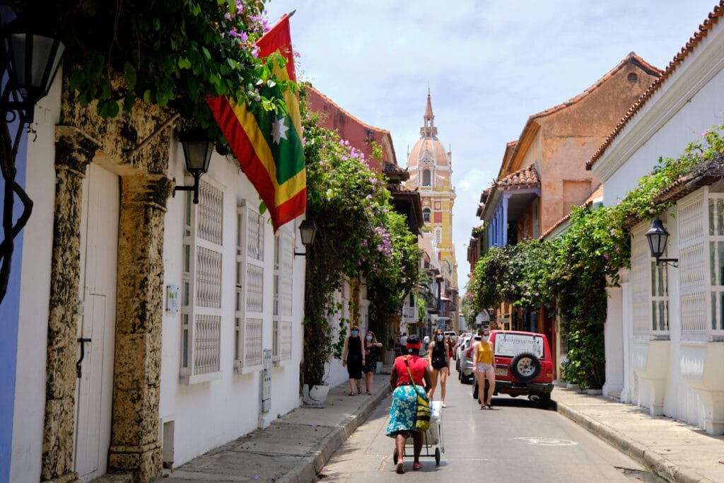 Photo of people walking on the streets of Cartagena, Colombia with the cathedral spire in the background.