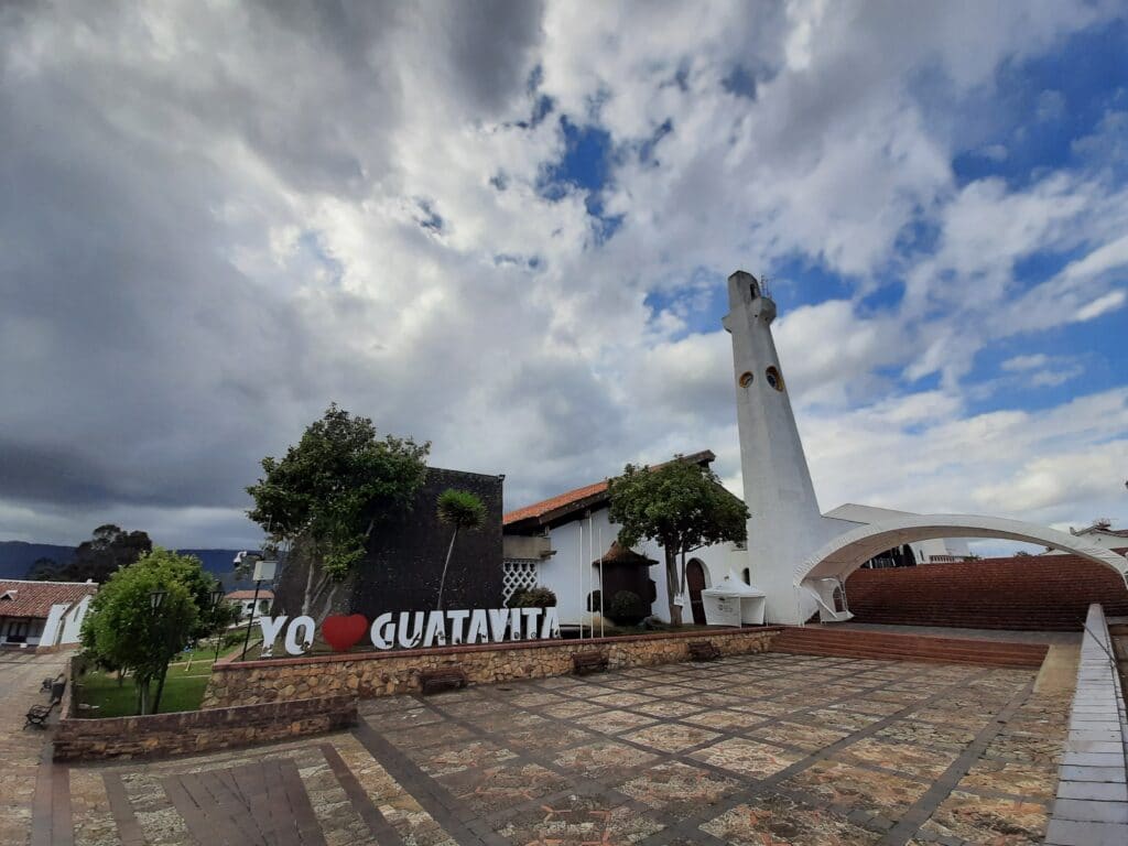 Photo of a plaza with a I love Guatavita sign and a church tower in the background.