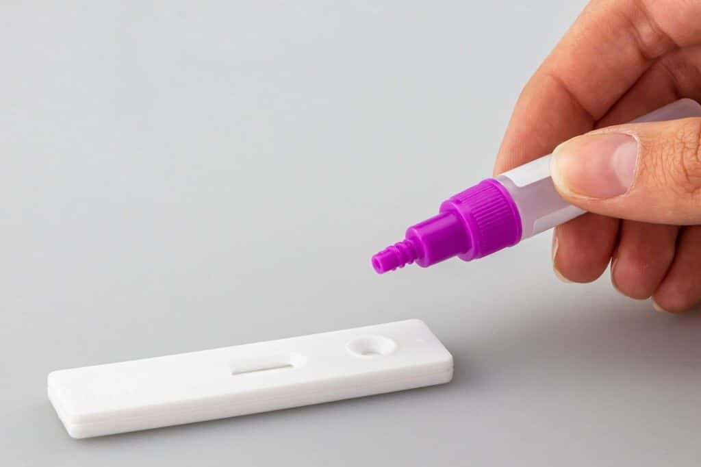 Photo of an at home Covid test kit with someone dropping liquid into the hole.