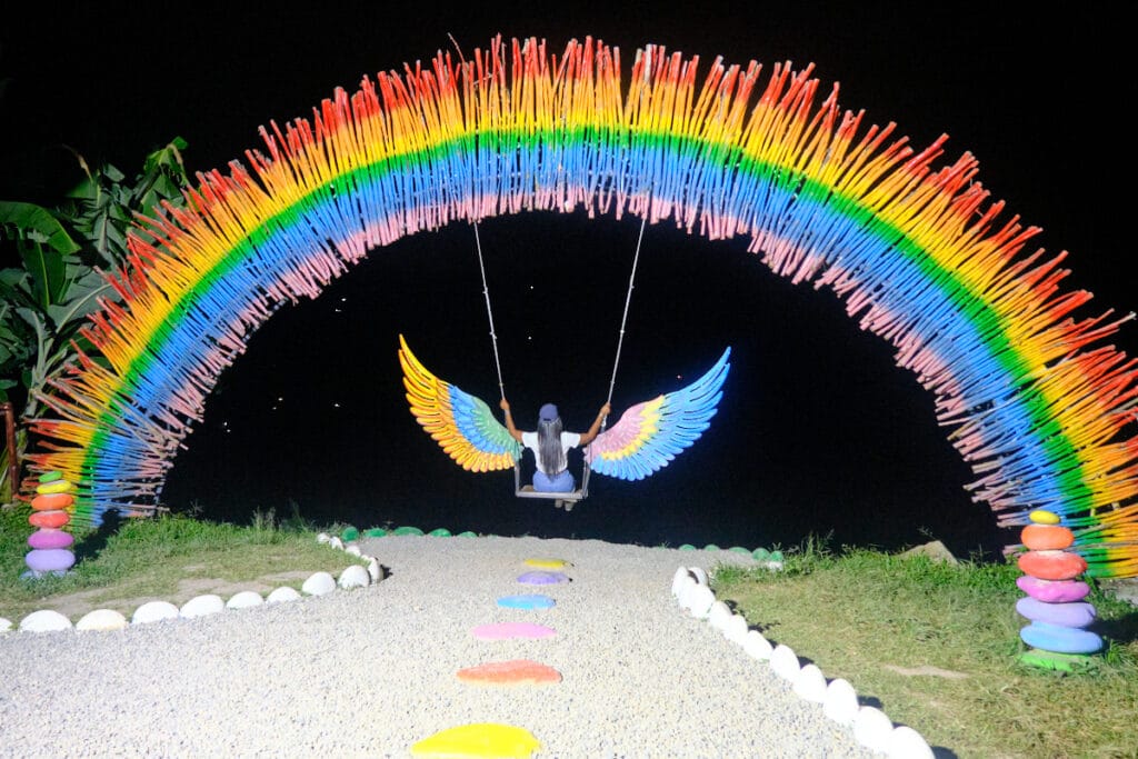 Photo of a girl in a swing with wings under an arch with the colors of a rainbow.