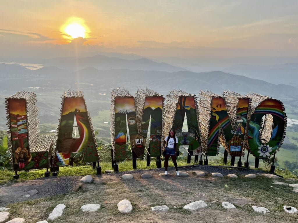 Photo of a girl standing in front of the letters that spell La Mano with the sunset behind.