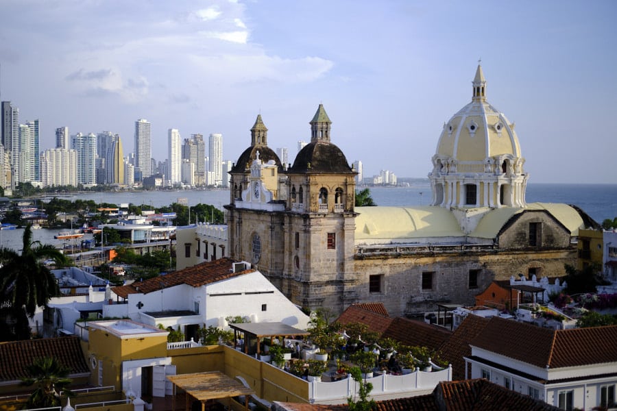 Photo of a church with two front towers and a large central dome and tower with skyscrapers and the ocean in the background seen after arriving from Santa Marta to Cartagena.