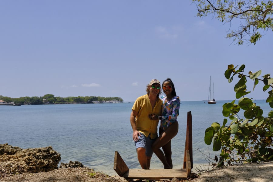 A couple walking up a small stairway from a beach in the Rosario Islands in Colombia with water and boats in the background.