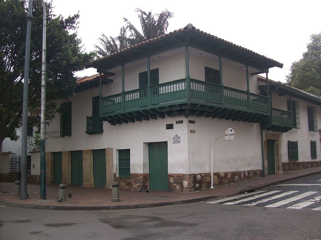 Photo of the building where the events of Colombian Independence Day occurred, on corner with white walls and green balconies and trim.