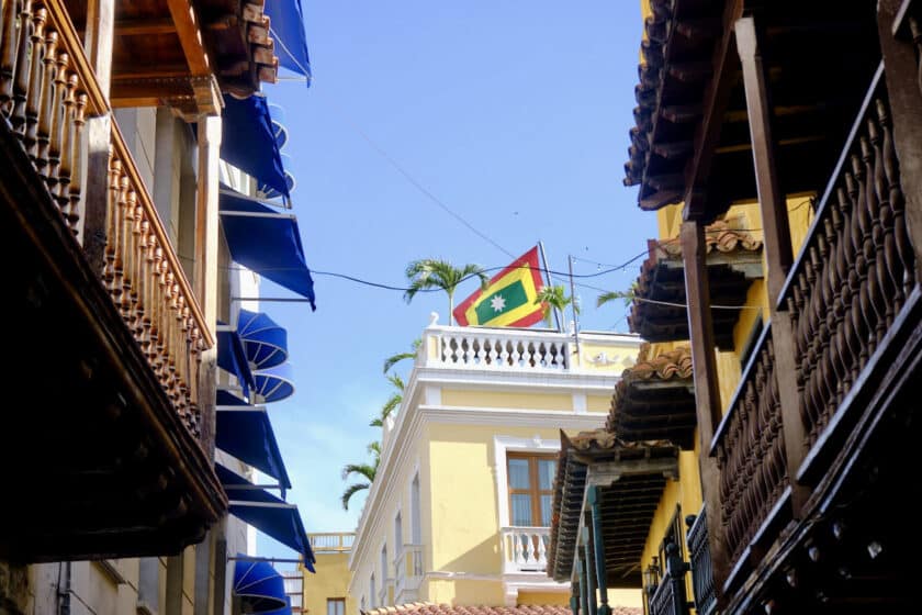 Photo of a flag with red, yellow, and green rectangles and a white star in the middle atop a building seen between balconies near some airbnbs in Cartagena, Colombia.