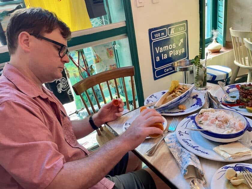 Photo of a guy putting hot sauce on his plate with other plates of food on a table at La Cevichería Cartagena.