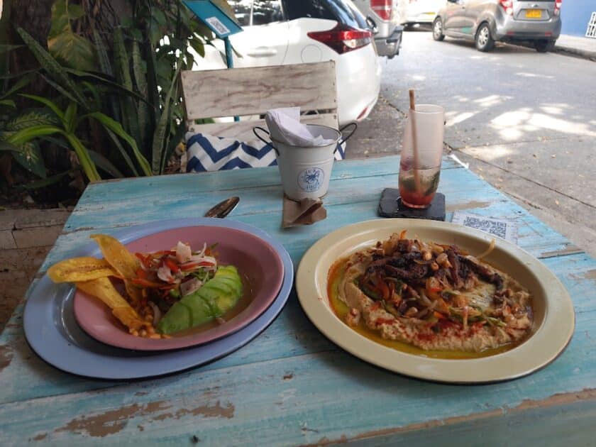 Photo of two plates, a drink, and napkins on a blue wooden table at La Vieja Guardia Fish & Beer in Cartagena.