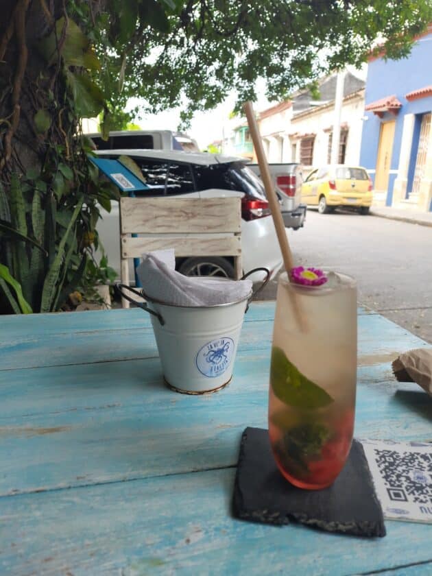 Photo of a drink on a table at Vieja Guardia Restaurant in Cartagena with a pail with napkins and a tree and cars parked on the street in the background.