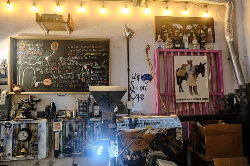 Photo of the inside of Cartagena's Café del Mural showing a coffee roaster, antiques, a chalk board with words about coffee, and old posters.
