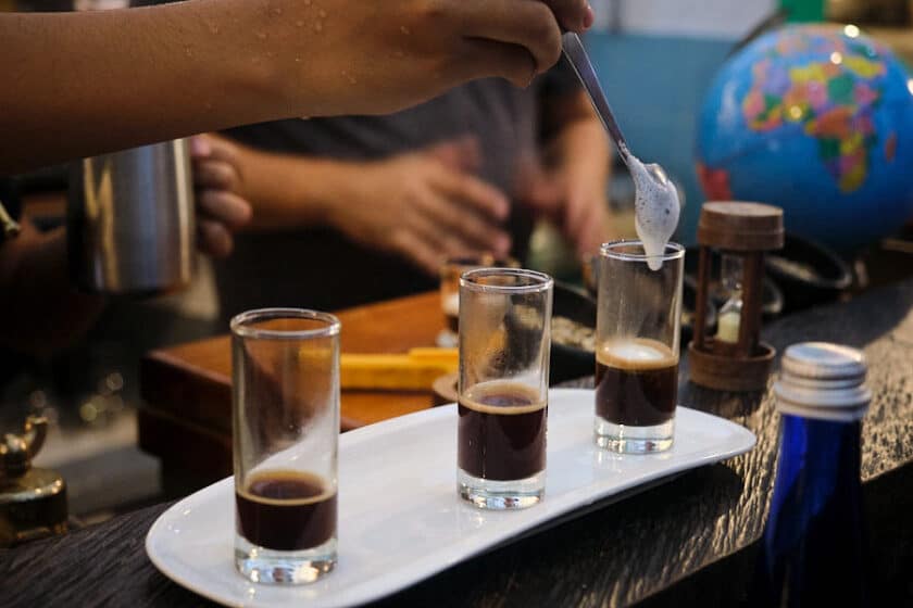 Photo of 3 shot glasses with coffee, with a spoon dropping milk into the one on the far right.