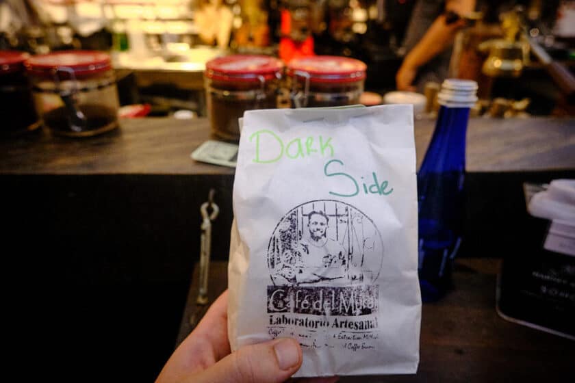 Photo of a bag of coffee with the words Dark Side written in green marker and a logo for Café del Mural showing a man making coffee.