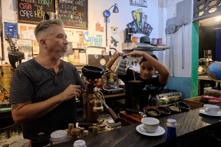 Photo of a girl pouring water from a kettle into a coffee maker while a man explains the process during a coffee tasting in Cartagena, Colombia.