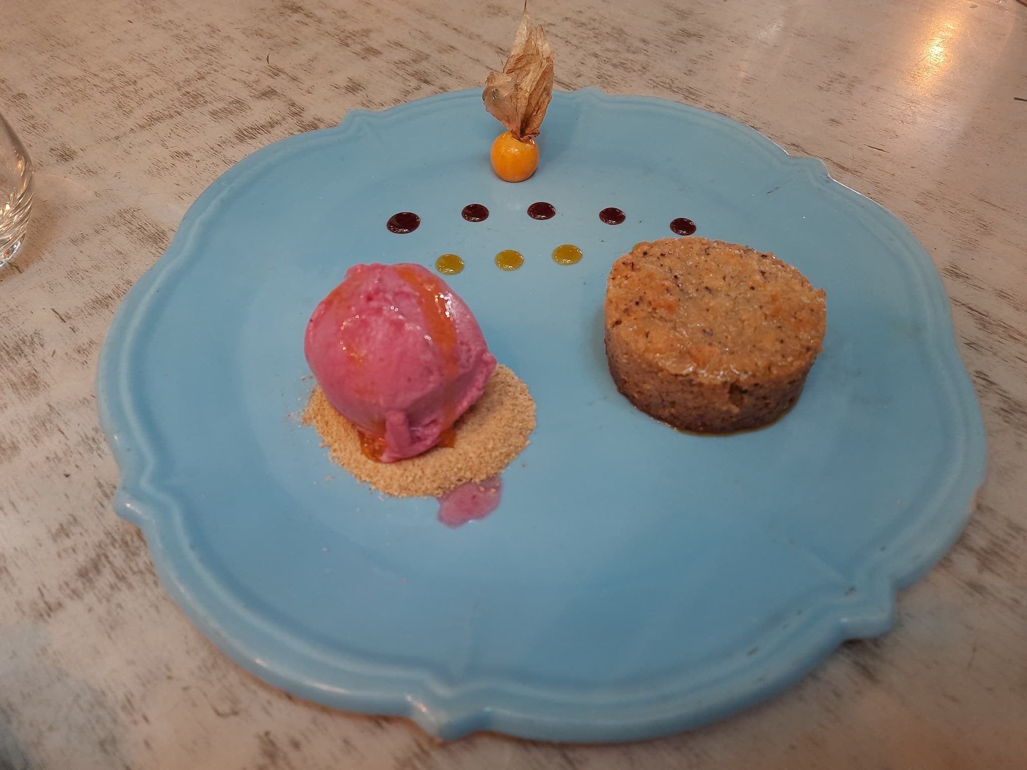 A pink ball of ice cream and a small pie on a teal plate.