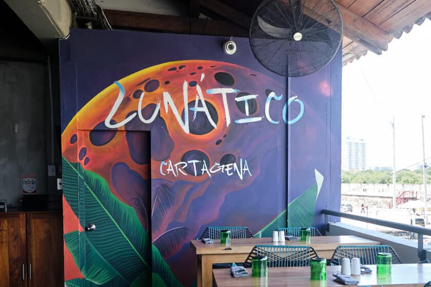 Wall with mural saying Lunático Cartagena behind some tables.