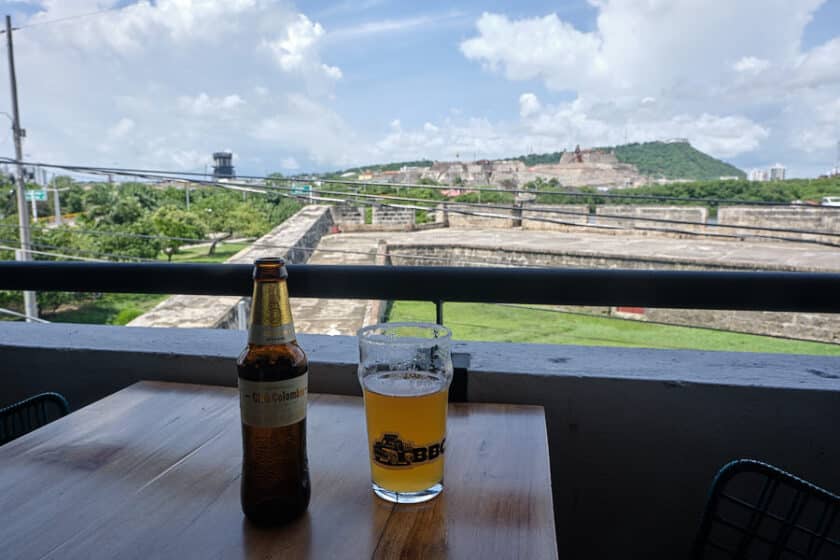 A glass and bottle of beer on a table with the Cartagena fort in the background.