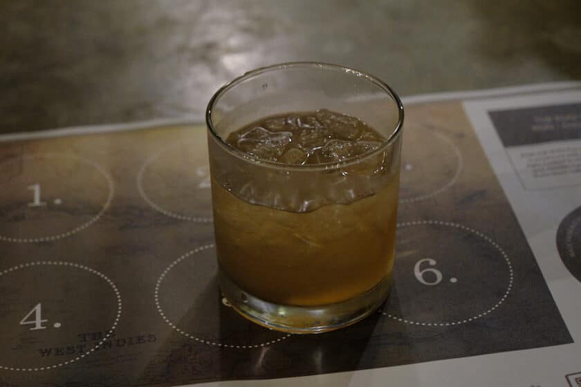 A glass with a brown liquid on a paper place mat with numbered places for glasses.