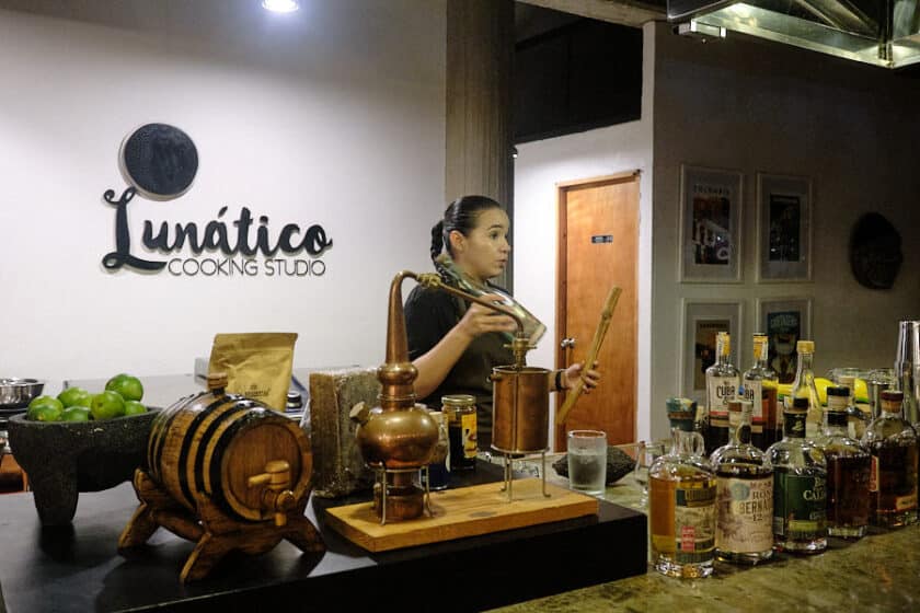 A woman holding a bottle and stick of sugar cane behind a bar while talking during a rum and chocolate tasting in Cartagena.