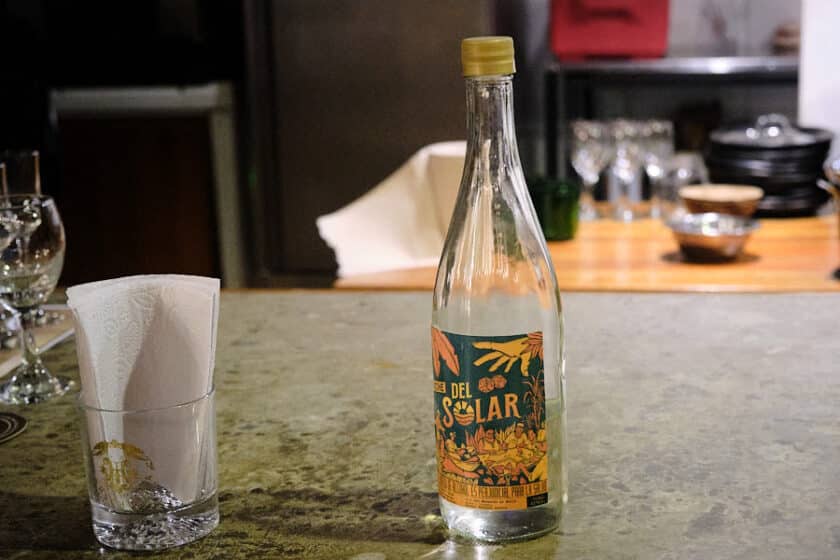 A clear bottle with a label that says del solar on a bar with a glass of napkins beside it.