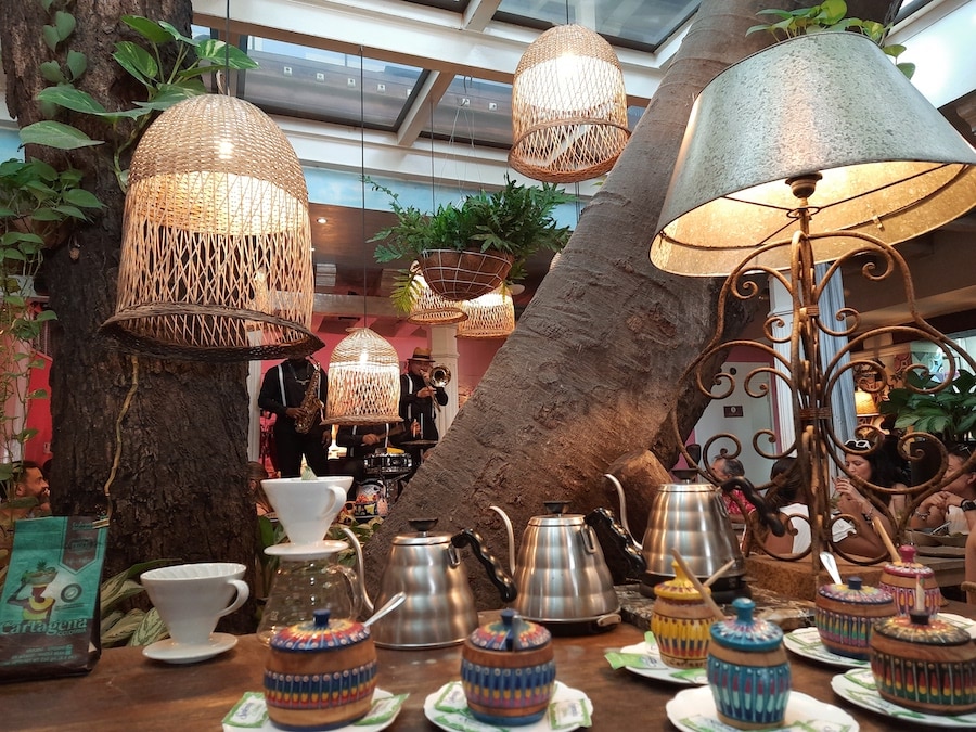 Coffee makers on a table with a tree behind it and a band on a stage behind it.