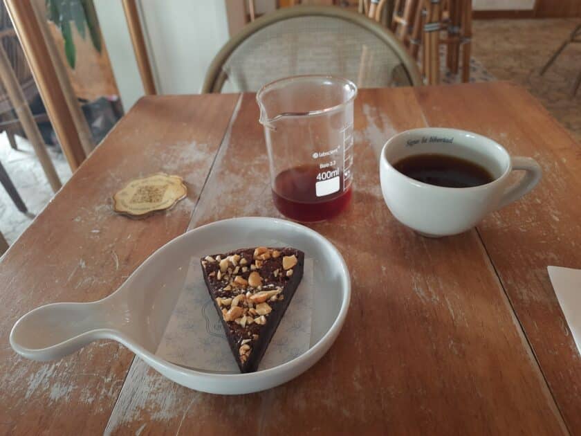 A cake with nuts, beaker with coffee, and mug with coffee on a wooden table.