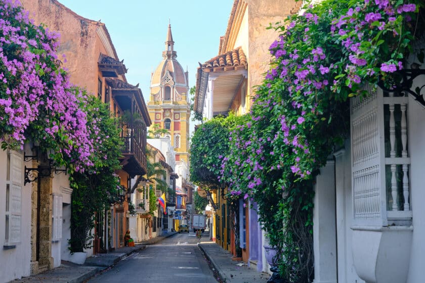 Street in Walled City Cartagena with cathedral in the background and flowers on buildings.