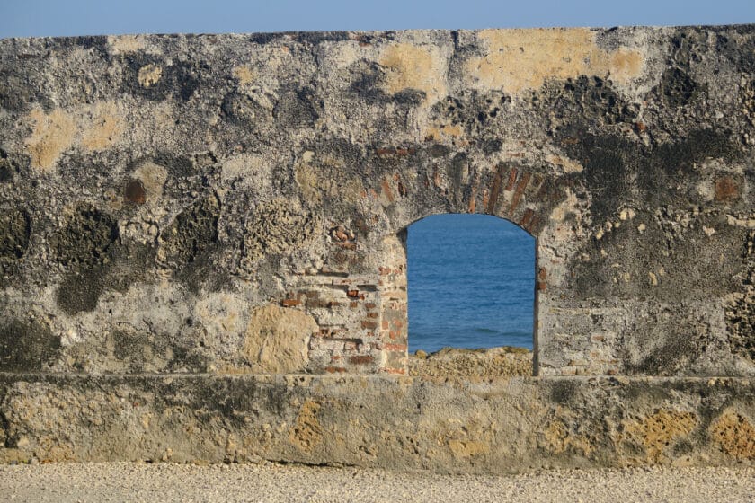 Photo of a small window in a stone wall looking out to sea.