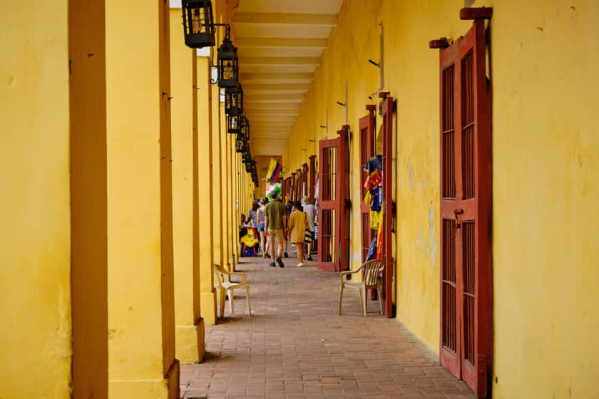 People walking between a yellow wall and columns in Cartagena, Colombia.