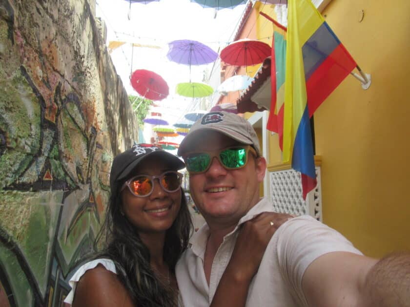 A couple taking a selfie on a narrow street with street art and umbrellas during a Cartagena 4 day itinerary.