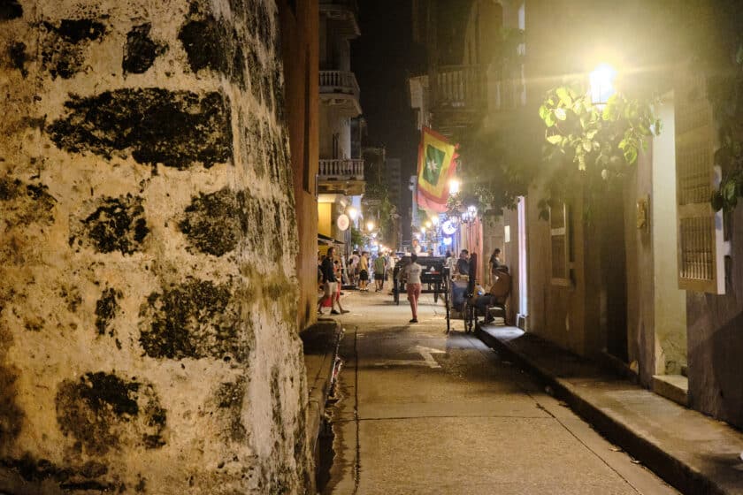 A narrow alleyway with people in a plaza during Cartagena NYE in the background.
